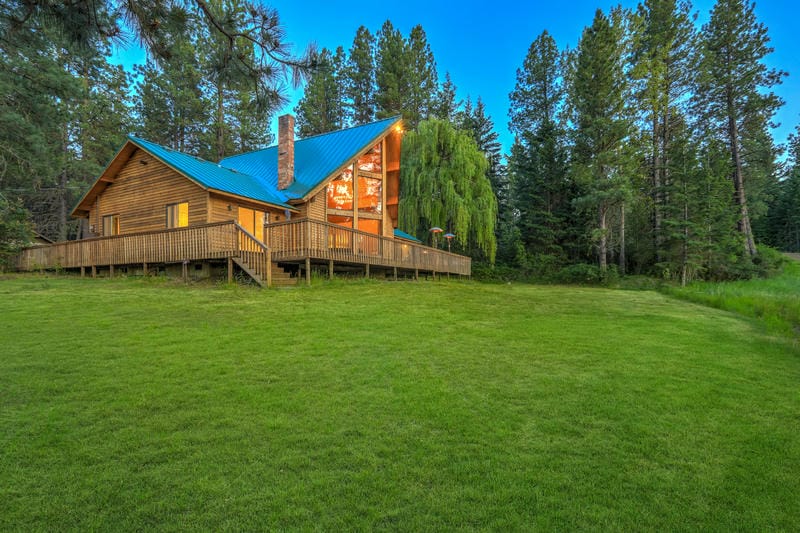 Nature with pine trees, mountains and beautiful chalet cider home exterior. Healthy Montana pasture after weed management